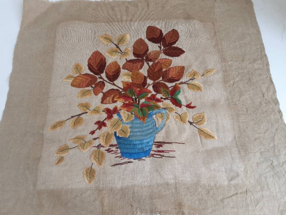A Vintage Embroidery Of A Blue Vase With An Arrangement Of Autumnal Leaves.
